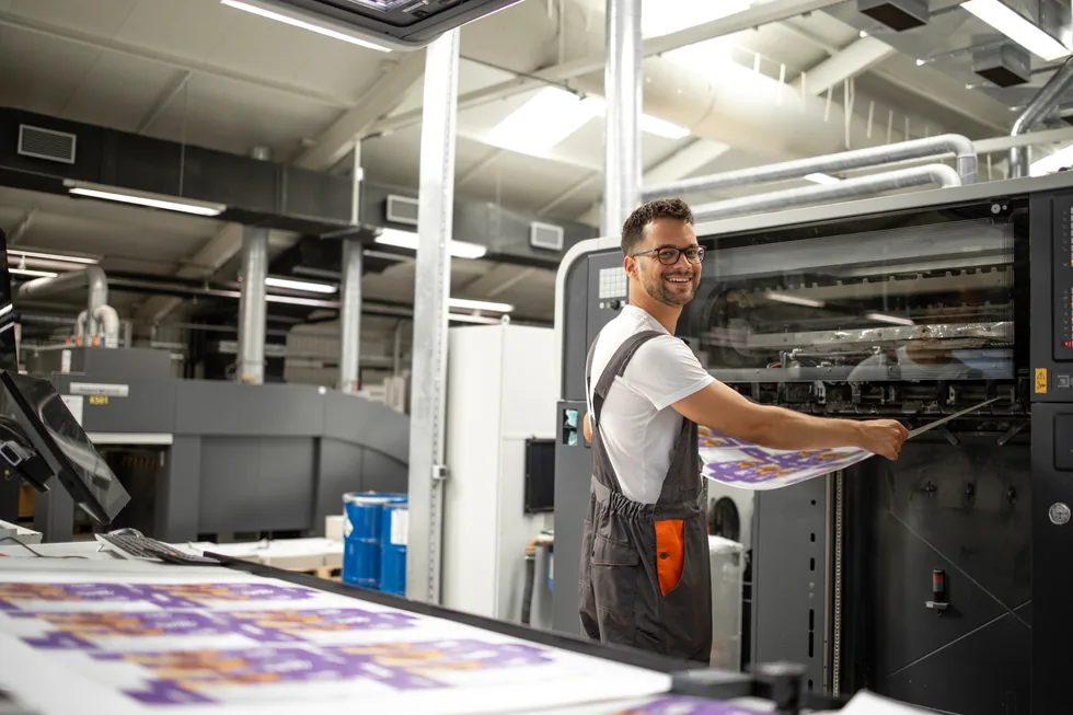 A press operator pulling a freshly printed sheet from a printing press
